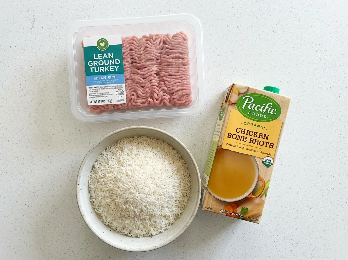 Top-down view of raw 93% lean ground turkey, dry jasmine rice, and high-protein bone broth.